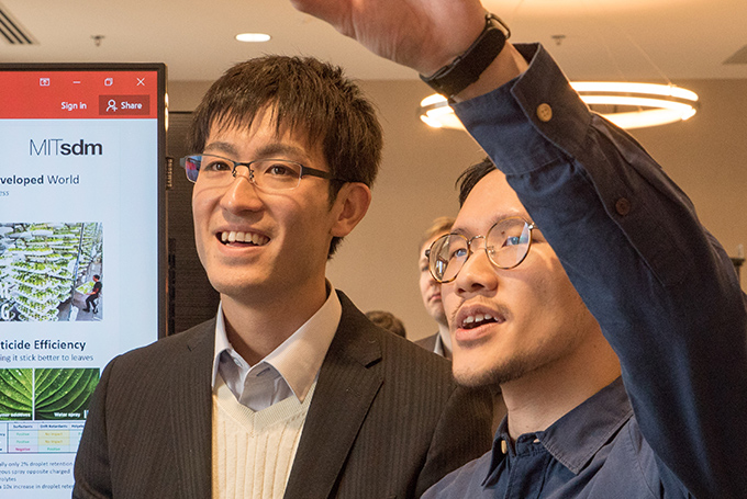 Two students look at a poster, one raising his arm to point at a part of it.