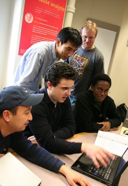 Five students gather around a laptop