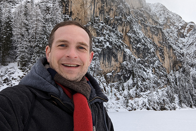 Chad Holmes stands in front of a snowy mountain peak.