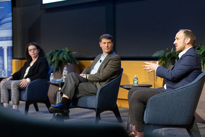 Megan Mitchell and J. Robert Wirthlin watch as Robert Plummer gestures while speaking.