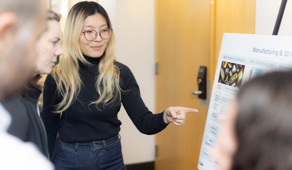 A student points at a poster on an easel with others pointing at it.