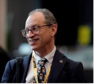 A man wearing glasses and a suit with a yellow lanyard around his neck.