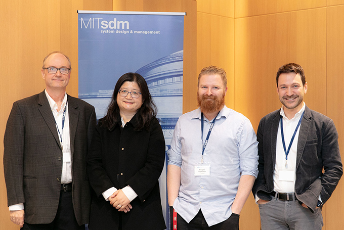 John Hajdukiewicz, Charlotte Wang, Doug Hamilton, and Nick Borge stand together in front of a pop-up banner with the SDM logo. They all smile for the camera.