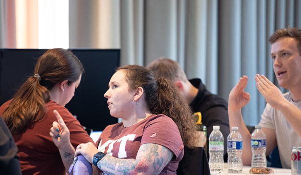 One woman wearing an MIT tee shirt describes something to another woman, who is facing away from her.